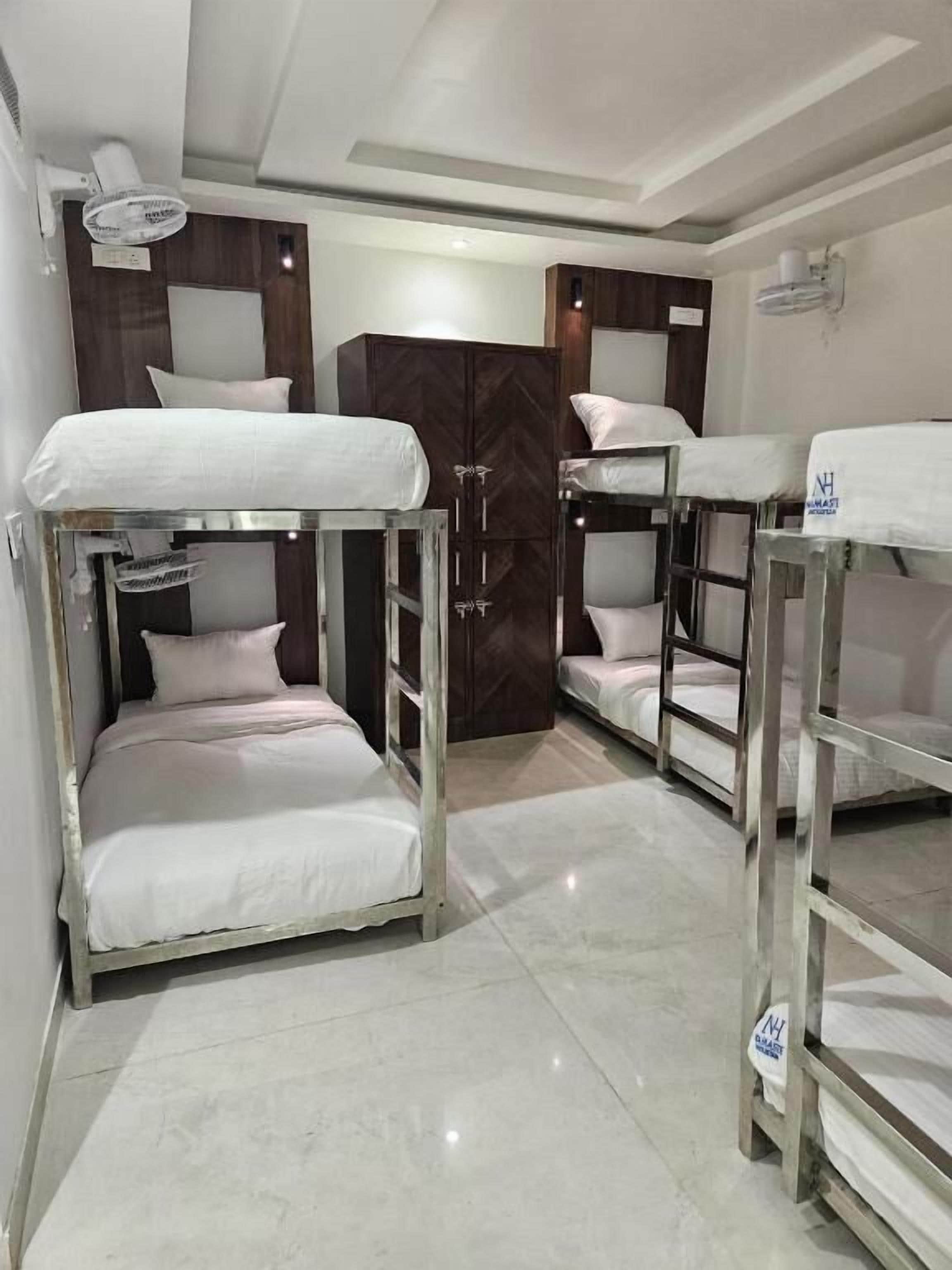 Une chambre d’hôtel avec des lits superposés, une armoire en bois et un ventilateur de plafond.