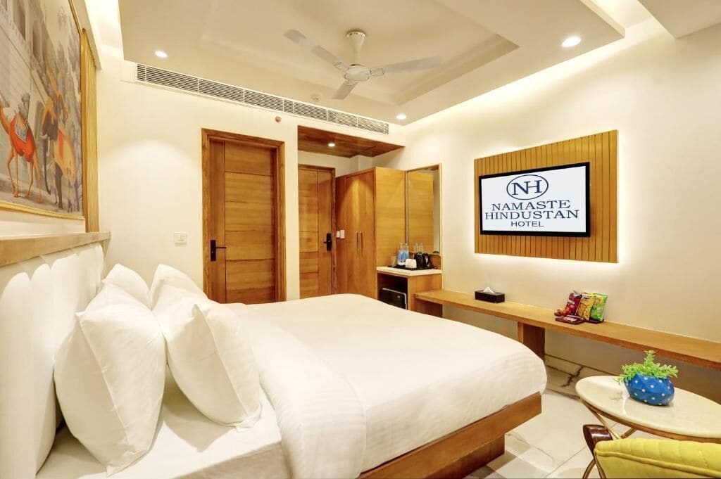 A modern hotel room with a large bed, wooden wardrobe, a small table, and a ceiling fan.