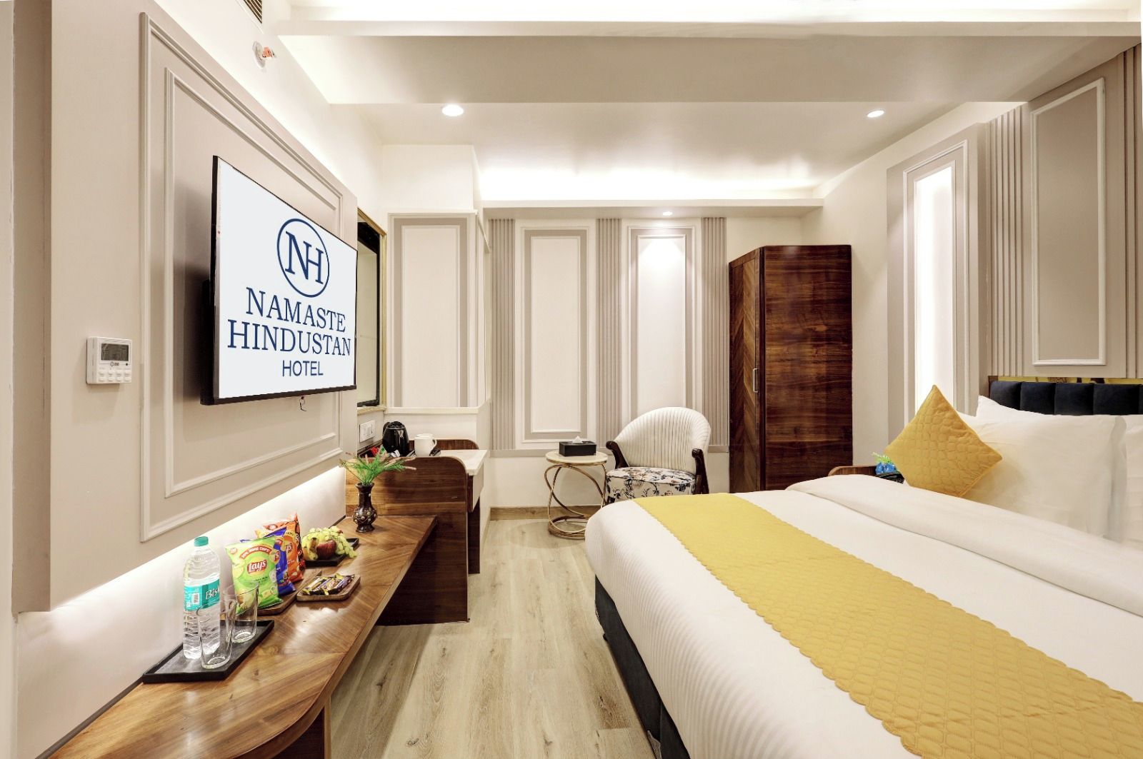 A hotel room with a bed, a desk with snacks, a TV, and a wardrobe.