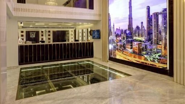 Een luxueuze hotellobby met een moderne kroonluchter, een groot digitaal scherm met een stadsbeeld en een marmeren receptiebalie.