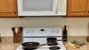 A kitchen with a white stove, a microwave above it, wooden cabinets, and a granite countertop.