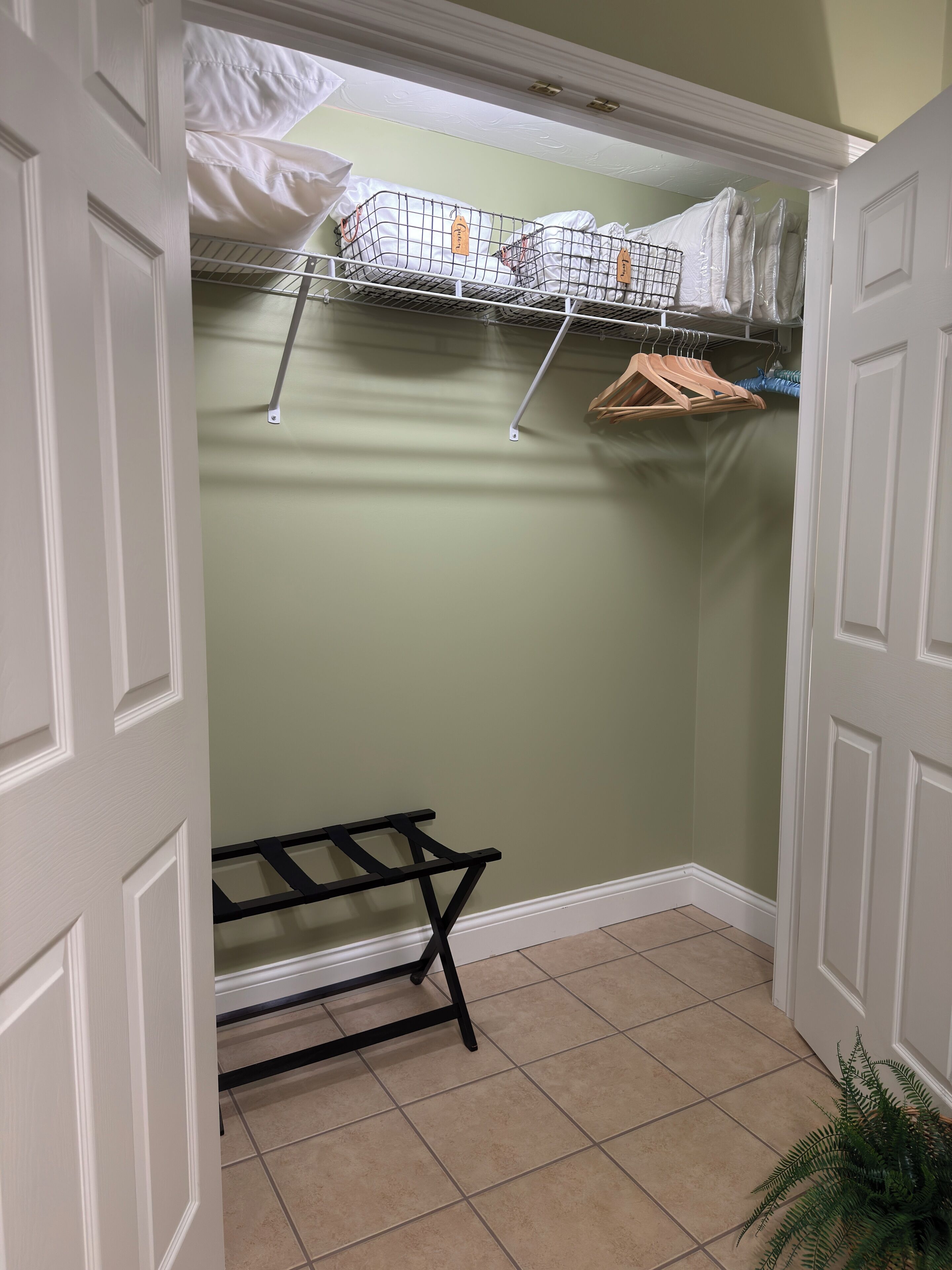 A walk-in closet with a metal drying rack, hanging clothes, and a shelf with folded items.