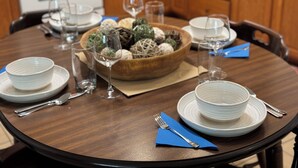 A round dining table with white plates, silverware, and a bowl of decorative items.