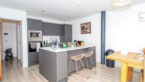 Une cuisine moderne avec des meubles gris, un four à micro-ondes et un évier. On y trouve un petit îlot avec des tabourets de bar et une table à manger avec des chaises.