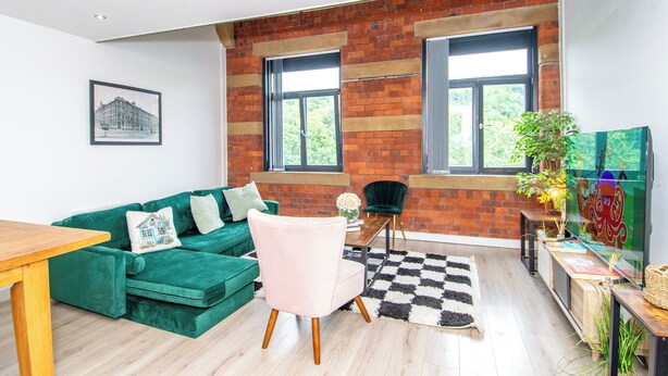 Un salon moderne avec un canapé vert, un fauteuil rose, une table en bois et un tapis à carreaux.