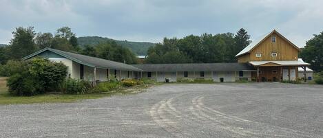 A motel with a gravel parking area, a covered outdoor seating area, and a large wooden building with a gabled roof.