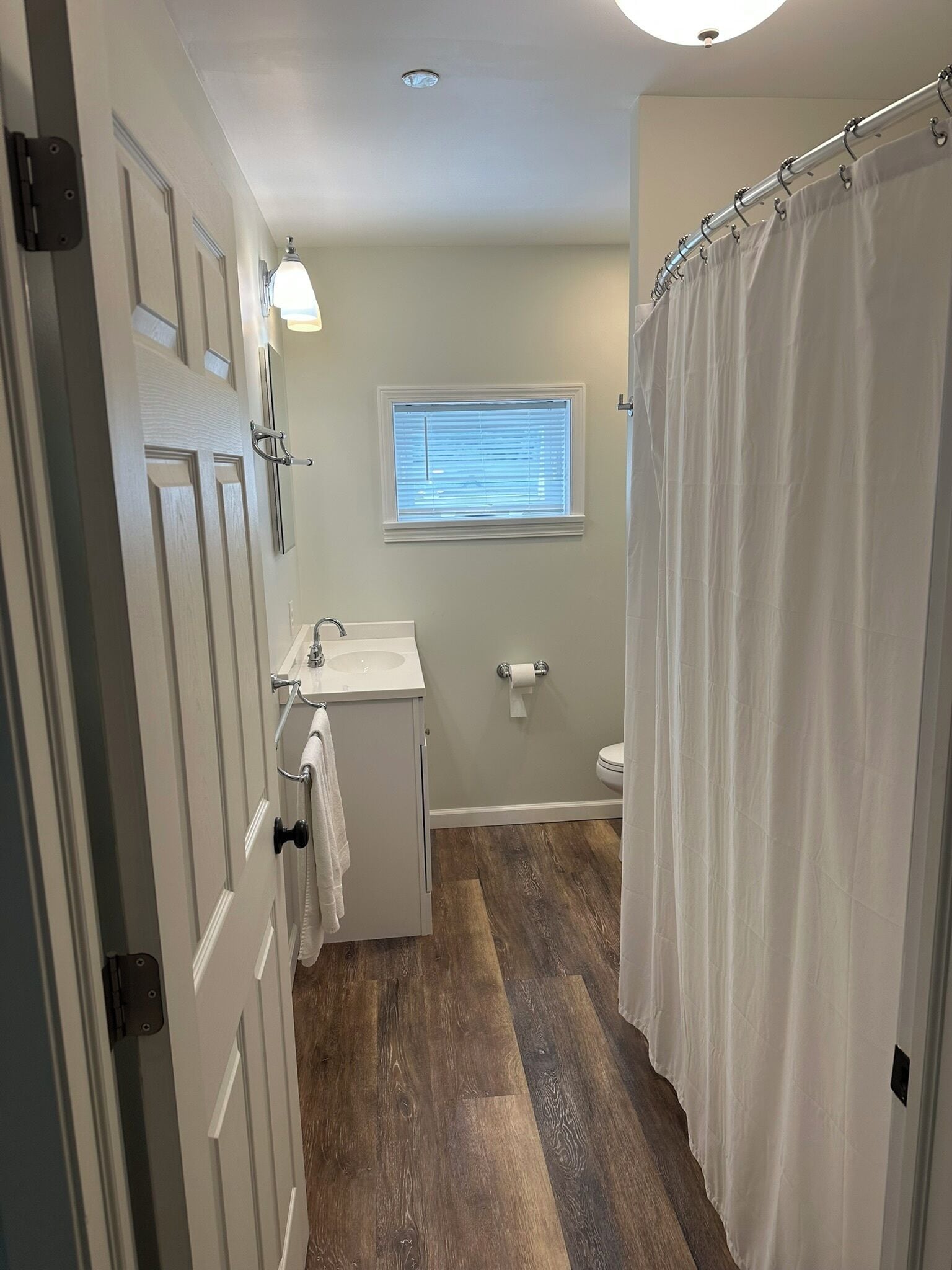 Un baño con piso de madera, un lavamanos, un inodoro y una cortina de ducha.