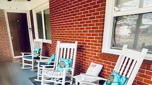 Une véranda avec trois fauteuils à bascule, chacun muni d’un coussin, adossée à un mur de briques.