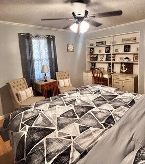 A bedroom with a bed, two chairs, a desk, a ceiling fan, and a wall with framed pictures. - Spacious family beach home wgrill,arcade, pool table,pingpong, gameroom,fire pit (Gulfport)