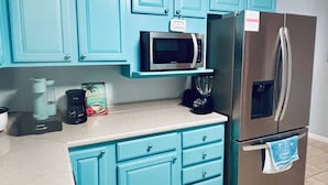 Une cuisine avec des armoires de couleur turquoise, un four à micro-ondes, une machine à café et un réfrigérateur.