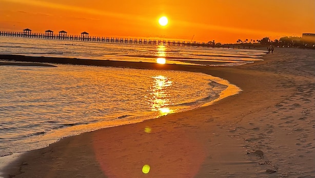 Une plage au coucher du soleil, avec le soleil qui se reflète sur l’eau.