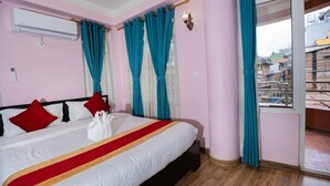 Ein Hotelzimmer mit einem Bett, roten und weißen Kissen, einer weißen Decke mit rotem und gelbem Streifen und einem Fenster mit blauen Vorhängen.