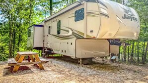 Un camping-car Jayco Eagle est stationné dans une zone boisée, à proximité d’une table de pique-nique.
