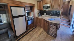 Une cuisine de taille réduite, dotée de meubles en bois, d’un four à micro-ondes encastré, d’une cuisinière et d’un évier.