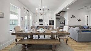 Un vaste espace de salle à manger avec une grande table en bois dressée pour un repas, une cuisine moderne en arrière-plan et un escalier menant à un niveau supérieur.