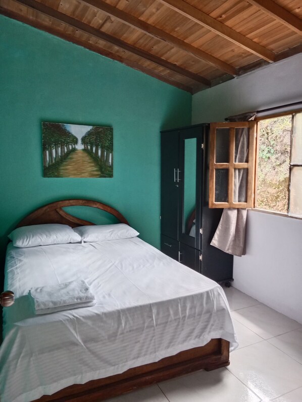 A bedroom with a bed, a wardrobe, a window, and a painting on the wall.