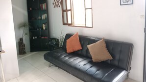 Ein Wohnzimmer mit einer schwarzen Ledersofa, einem Bücherregal und einem Fenster mit Holzrahmen.
