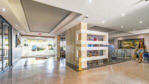 Un lobby espacioso con diseño moderno, que incluye un mostrador de recepción, una entrada de cristal y una pared decorativa con estanterías.