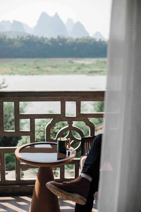 A table with a cup and saucer on a balcony overlooking a river and mountains. - YangShuo Percent Hotel (Guilin)