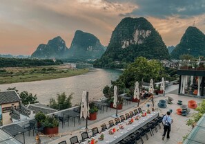 A riverside restaurant with outdoor seating overlooking a river and mountains. - YangShuo Percent Hotel (Guilin)