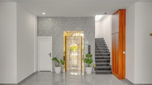 A modern hallway with a marble floor, a wooden staircase, and two potted plants. - Soho Villa&Resort (Khemarak Phoumin)