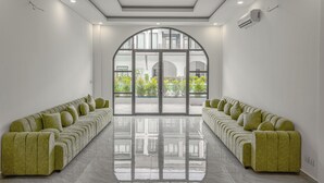 A modern hotel lobby with a long, green upholstered sofa facing a large arched glass door leading outside. - Soho Villa&Resort (Khemarak Phoumin)