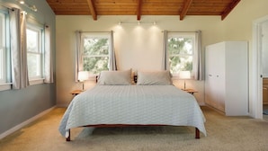 A bedroom with a large bed, two windows with curtains, a wardrobe, and a ceiling with wooden beams. - Sunset Orchard- Sunny side of Waimea, close to beaches! (Waimea)
