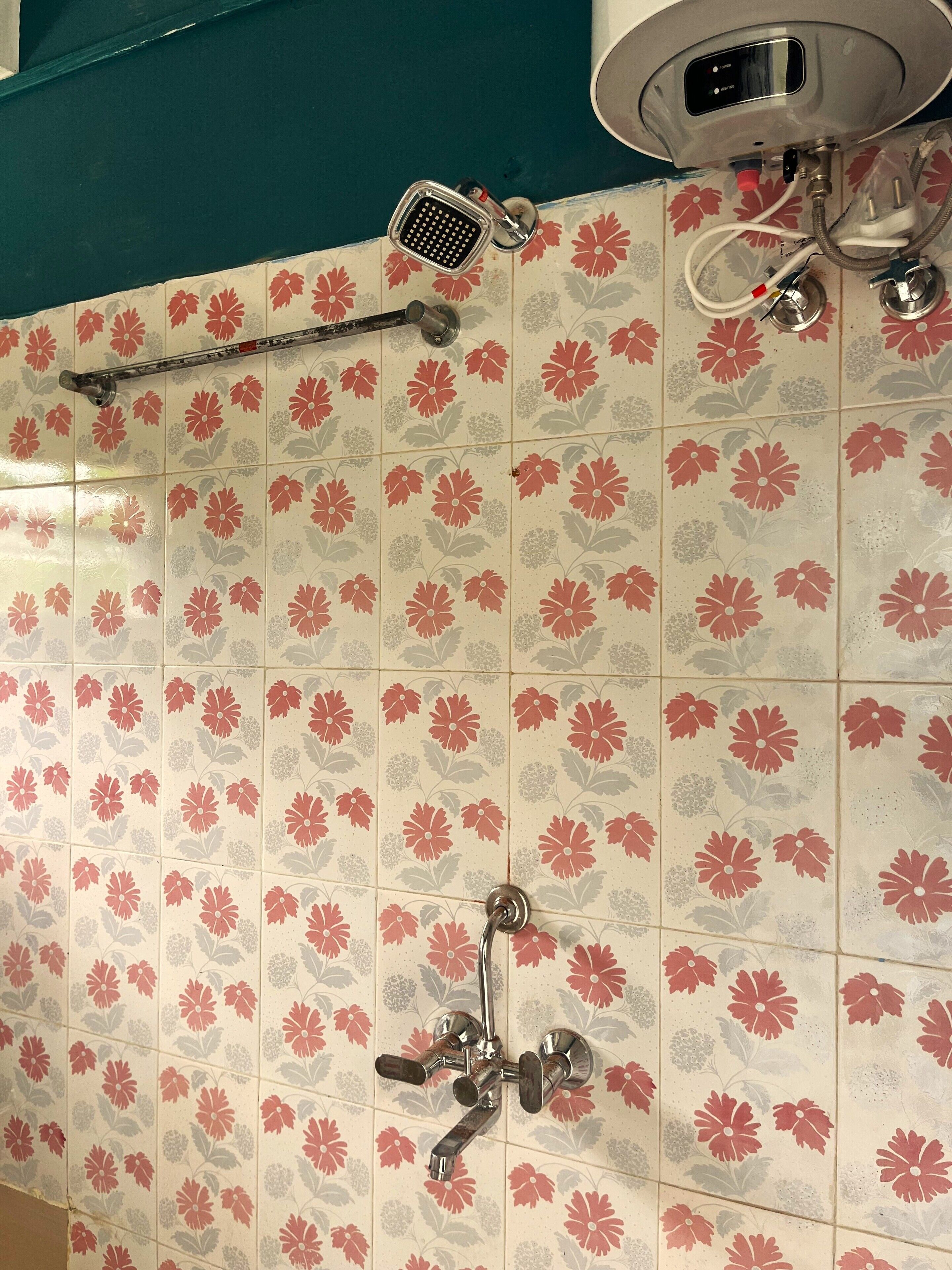 A bathroom with floral-patterned tiles, a handheld showerhead, a fixed showerhead, and a wall-mounted faucet.