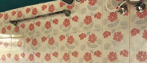 A bathroom with floral-patterned tiles, a handheld showerhead, a fixed showerhead, and a wall-mounted faucet.