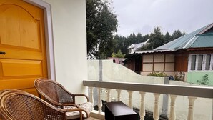A balcony with wicker chairs and a small table, overlooking a residential area with houses and trees.