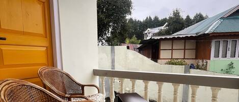 A balcony with wicker chairs and a small table, overlooking a residential area with houses and trees.