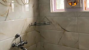 A bathroom with a white marble wall, a window with a fan, and a shower with a handheld showerhead.