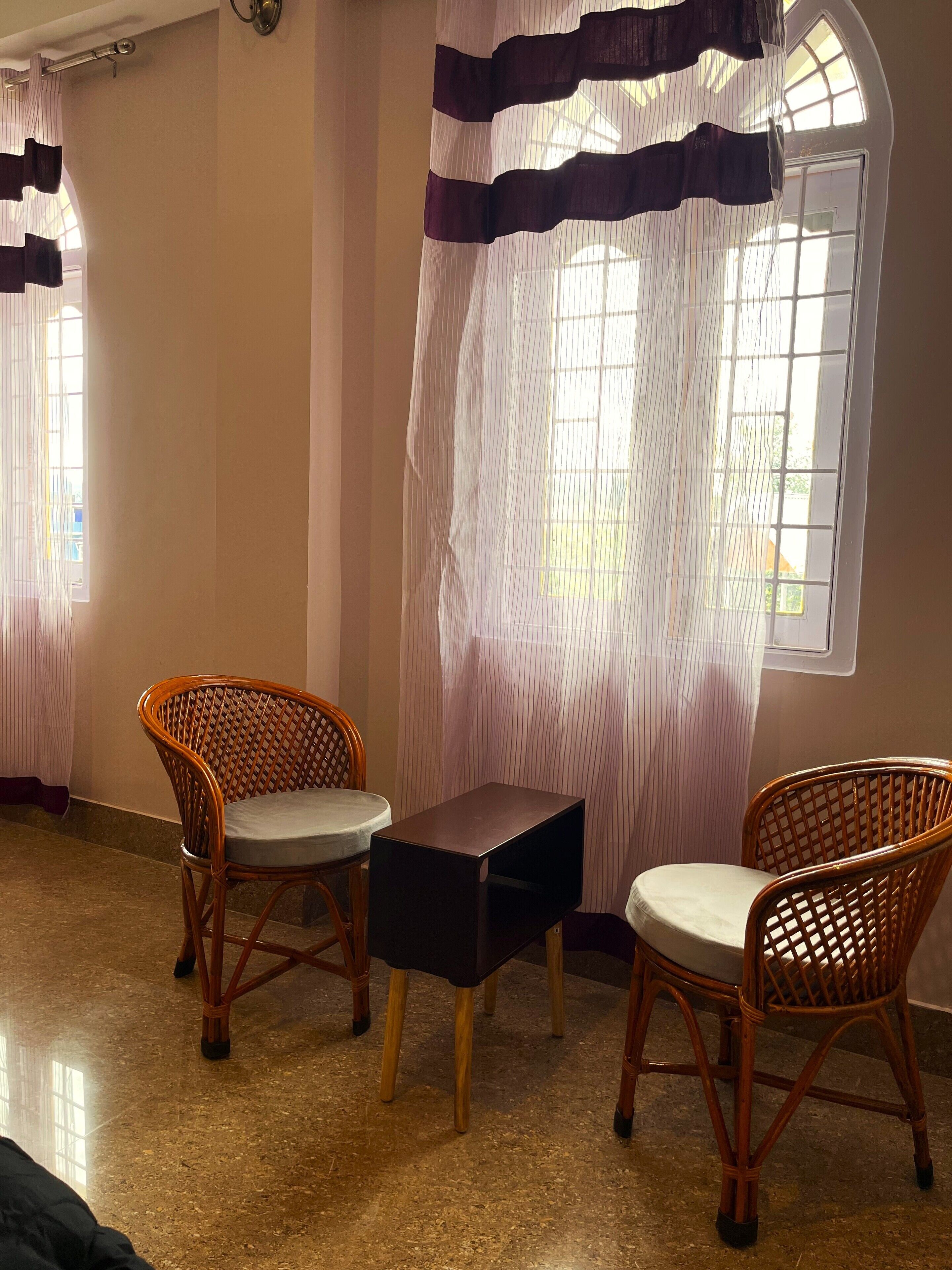 A room with two wicker chairs, a small table, and a window with striped curtains.