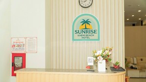 En receptionsdisk med en klocka, en skylt för Sunrise Khem Beach Hotel, en brandsläckare och en blomvas.