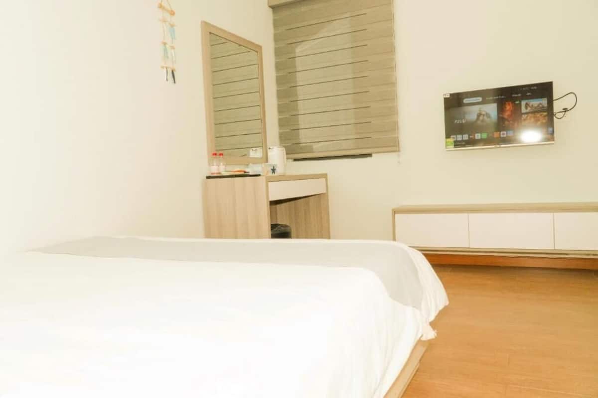 Un dormitorio con cama, mesita de noche, espejo, ventana con persianas y televisor montado en la pared.