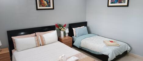 A hotel room with two beds, a nightstand with a lamp, and two framed artworks on the walls.