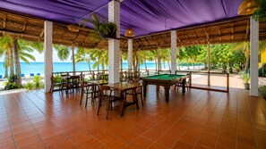 Ein Billardtisch-Bereich im Innenbereich mit Blick auf den Strand, umgeben von Tischen und Stühlen.