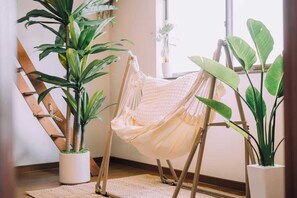 Una silla hamaca en una habitación con plantas grandes en macetas y una escalera de madera.