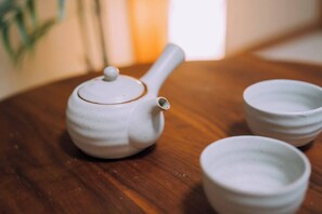 Una tetera blanca con tapa y pico sobre una mesa de madera. Hay dos tazas blancas al lado de la tetera.