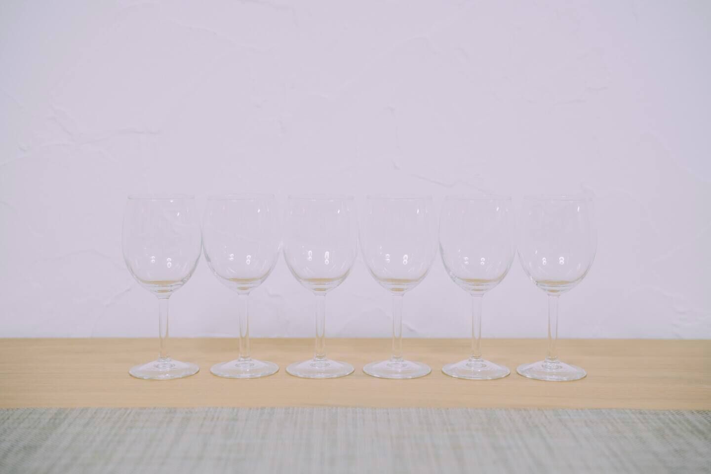 Cinq verres à vin vides sont alignés sur une surface en bois, devant un mur uni.