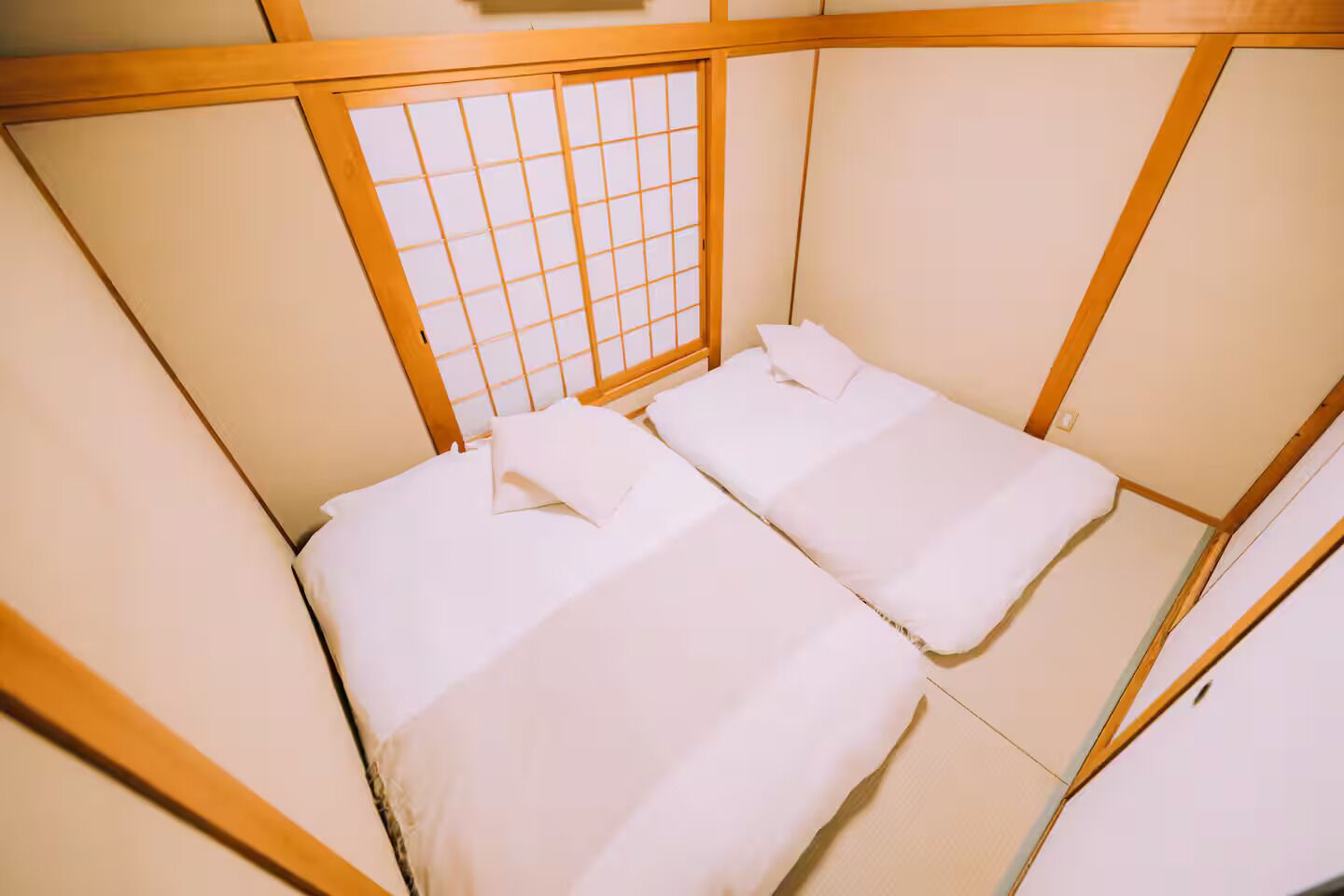 A traditional Japanese-style room with tatami mat flooring, a shoji screen, and two beds with white bedding.