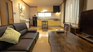 A compact living space with a sofa, a dining table, a kitchen area, and a television. - Stay in Miyashita (Asahikawa)
