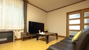 A living room with a sofa, a flat-screen TV, a coffee table, and a wooden cabinet. - Stay in Miyashita (Asahikawa)