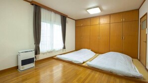A room with wooden flooring, a bed with white bedding, a heater, and a window with curtains. - Stay in Miyashita (Asahikawa)
