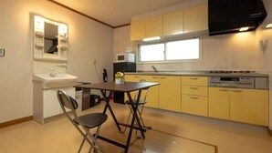 A compact kitchen with a sink, microwave, and stove. There is a small dining table with two chairs. - Stay in Miyashita (Asahikawa)