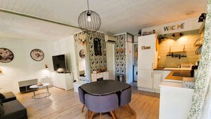 A modern kitchen with a 'Welcome' sign, a dining area with a round table, and a living room with a sofa and a TV.