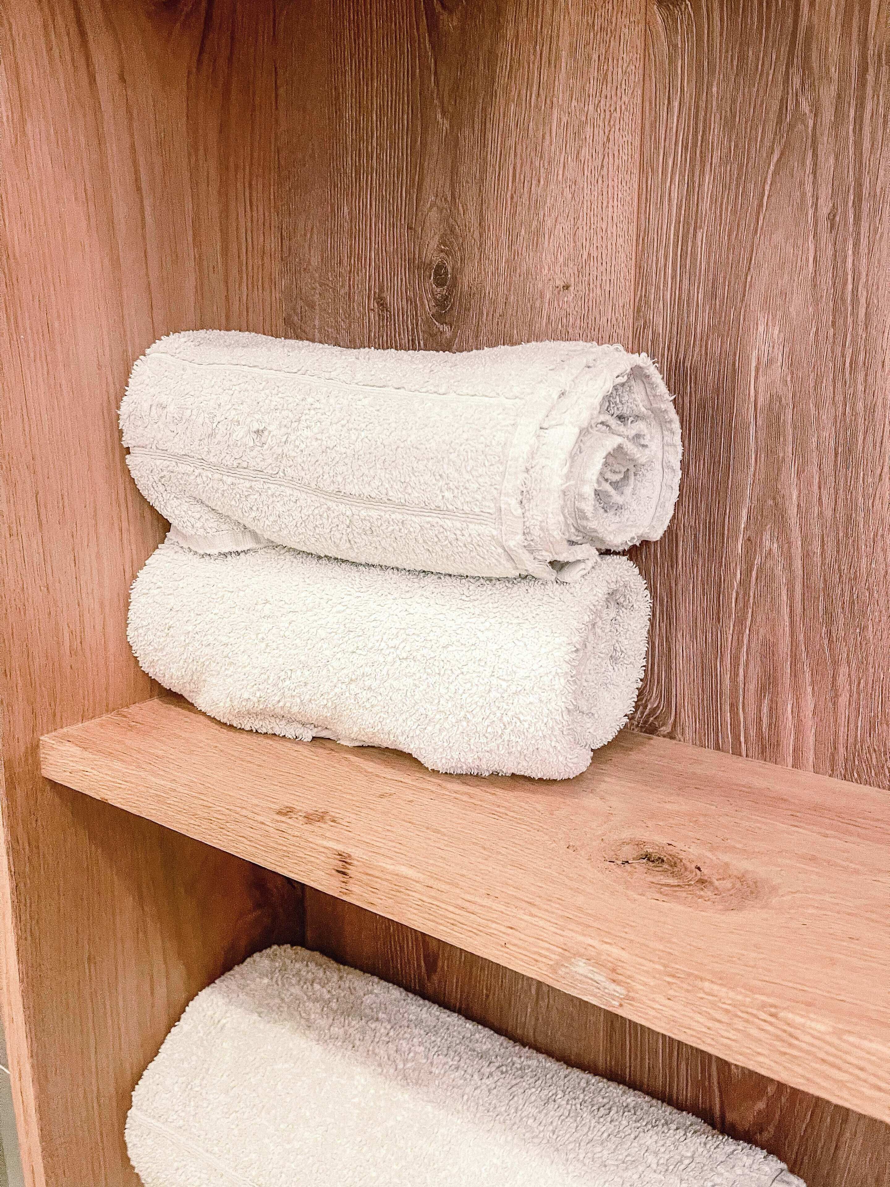Ein Holzregal mit zwei aufgerollten weißen Handtüchern.