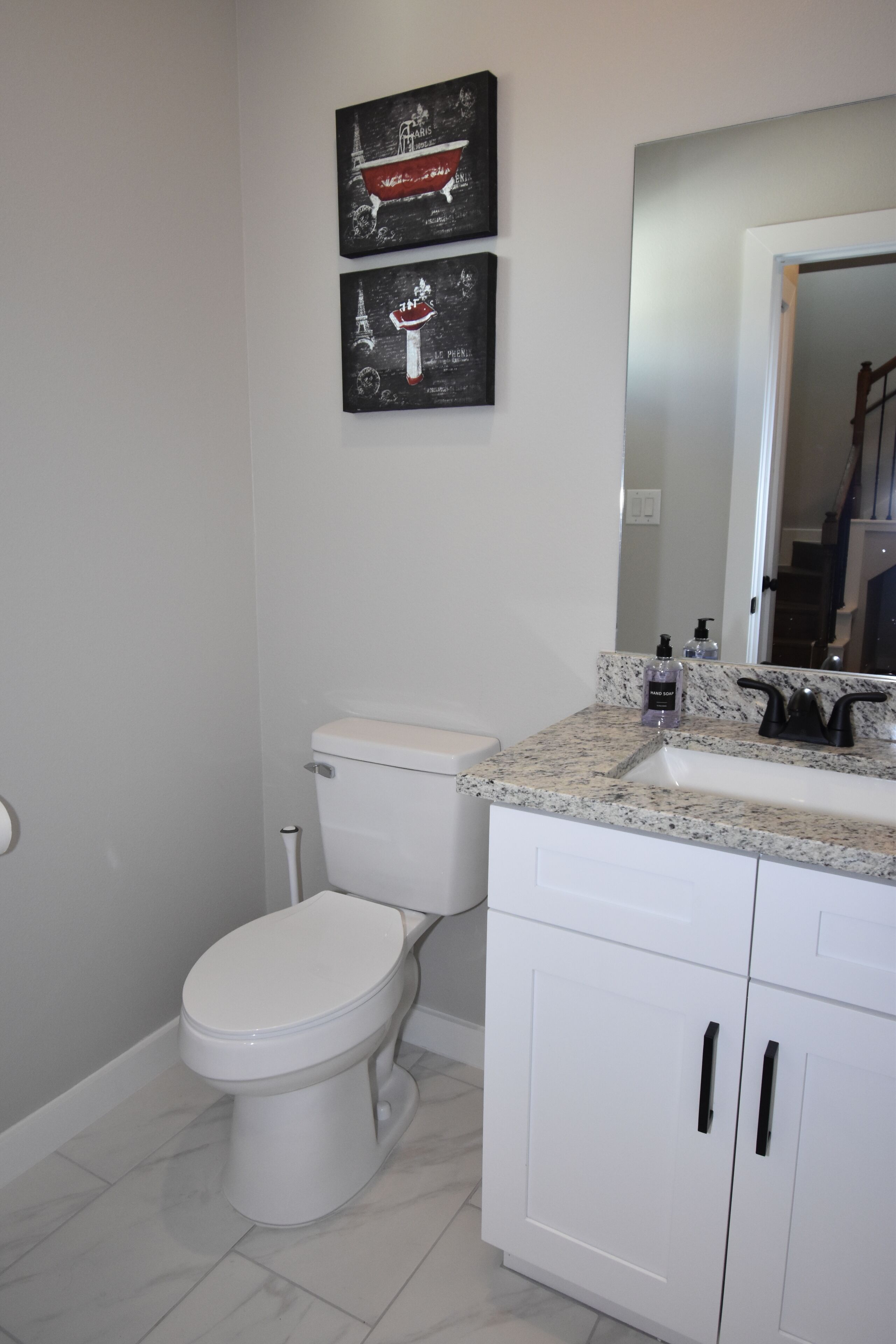 A bathroom with a white toilet, a granite countertop sink, and two framed pictures on the wall.