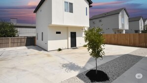 Una casa moderna de dos pisos con techo plano, un pequeño porche delantero y un árbol en el jardín.
