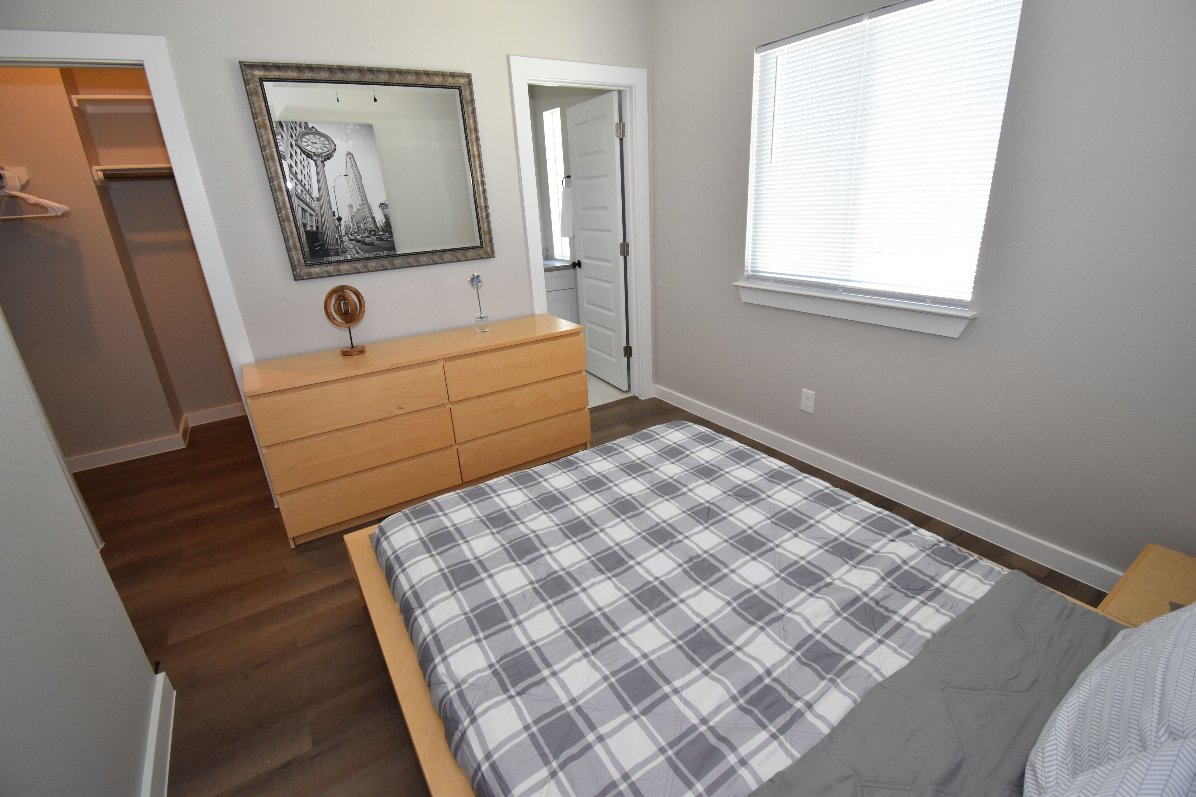 Un dormitorio con cama, cómoda, espejo y una puerta que da a otra habitación.